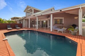 A swimming pool with a wooden deck, lounge chairs, and a covered patio area. - Villa Palmera - Four Bedroom Villa, Sleeps 8 (Saint-François)