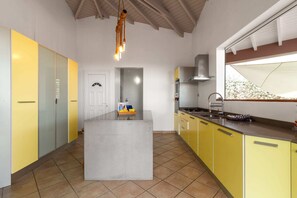 A kitchen with a central island, yellow cabinets, a stainless steel sink, and a window with a view. - Villa Palmera - Four Bedroom Villa, Sleeps 8 (Saint-François)