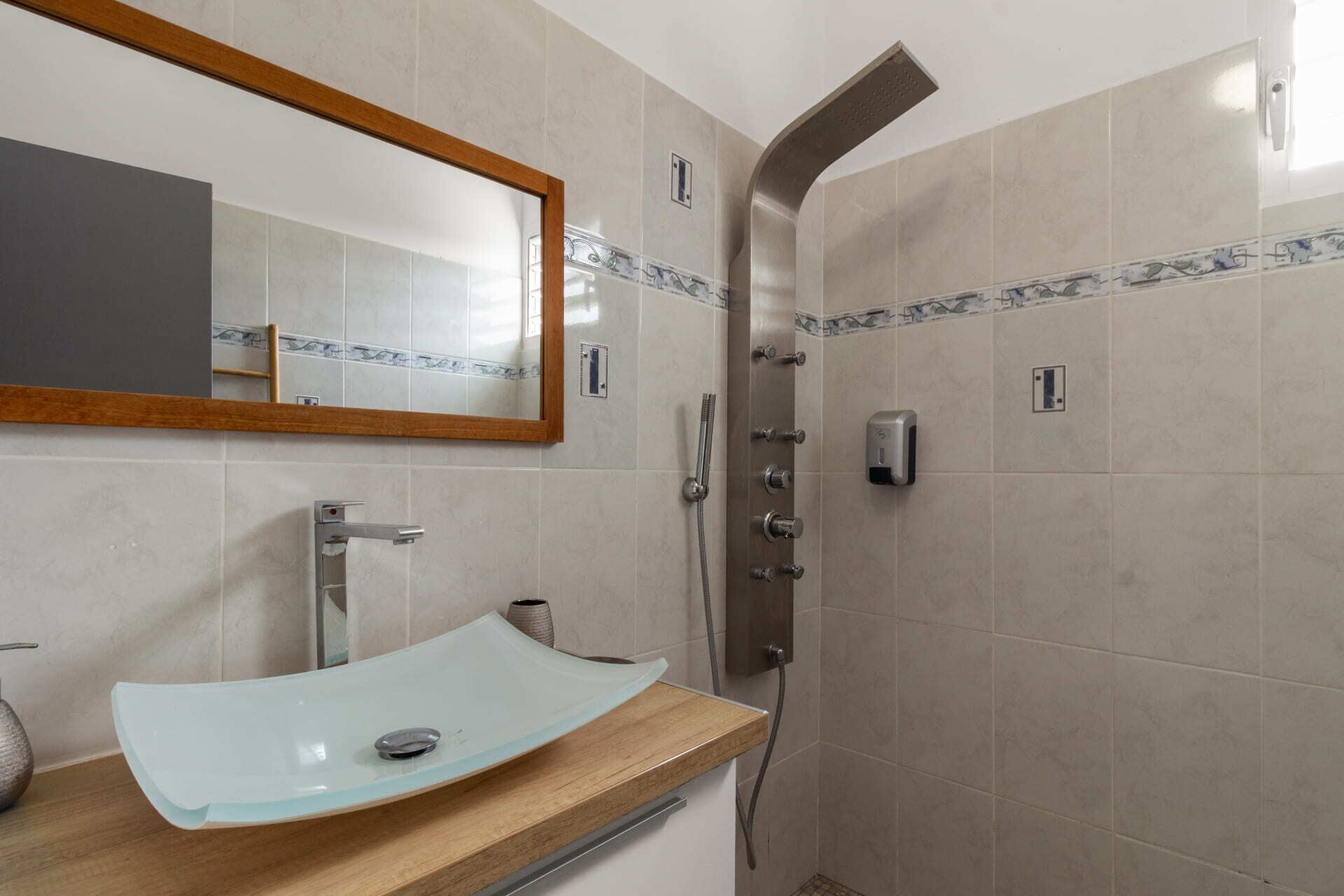 A bathroom with a sink, mirror, shower, and tiled walls.