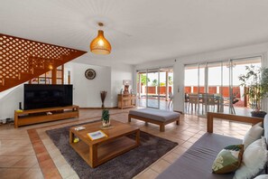 Een ruime woonkamer met een televisie, salontafel, bank en een trap.