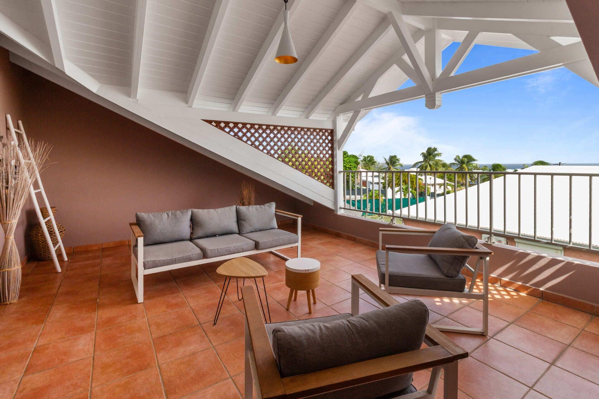 A spacious balcony with a sofa, chairs, and a small table, overlooking a pool and palm trees.
