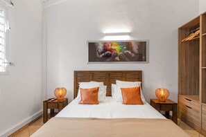 A bedroom with a bed, two bedside tables with lamps, a wooden headboard, a large abstract painting, and a wardrobe. - Villa Palmera - Four Bedroom Villa, Sleeps 8 (Saint-François)