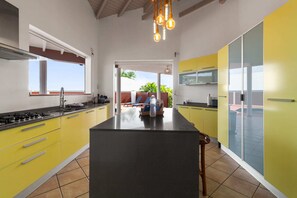 Una cuina moderna amb armaris grocs, una illa central i vistes a una zona exterior.