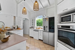 A modern kitchen with white cabinetry, stainless steel appliances, and a large window providing natural light. - Villa Zouina - Three Bedroom Villa, Sleeps 7 (Le Carbet)