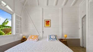 Et soveværelse med en stor seng, to sengeborde med lamper, et indrammet plakat på væggen og et vindue med udsigt til grønne omgivelser.