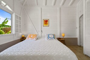 Ein Schlafzimmer mit einem großen Bett, zwei Nachttischlampen, einem gerahmten Poster an der Wand und einem Fenster mit Blick auf Grünflächen.