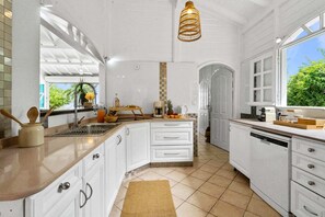 A kitchen with white cabinetry, a tiled backsplash, a hanging light fixture, and a window with a view of greenery. - Villa Zouina - Three Bedroom Villa, Sleeps 7 (Le Carbet)