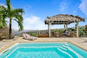 A pool area with a thatched gazebo, lounge chairs, and a palm tree. - Villa Zouina - Three Bedroom Villa, Sleeps 7 (Le Carbet)
