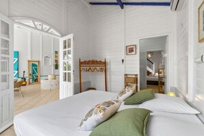 A bedroom with a bed, pillows, a wooden headboard, a wardrobe, and a doorway leading to another room. - Villa Zouina - Three Bedroom Villa, Sleeps 7 (Le Carbet)