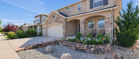 A two-story house with a stone facade, a garage, and a landscaped front yard with rocks and flowers.