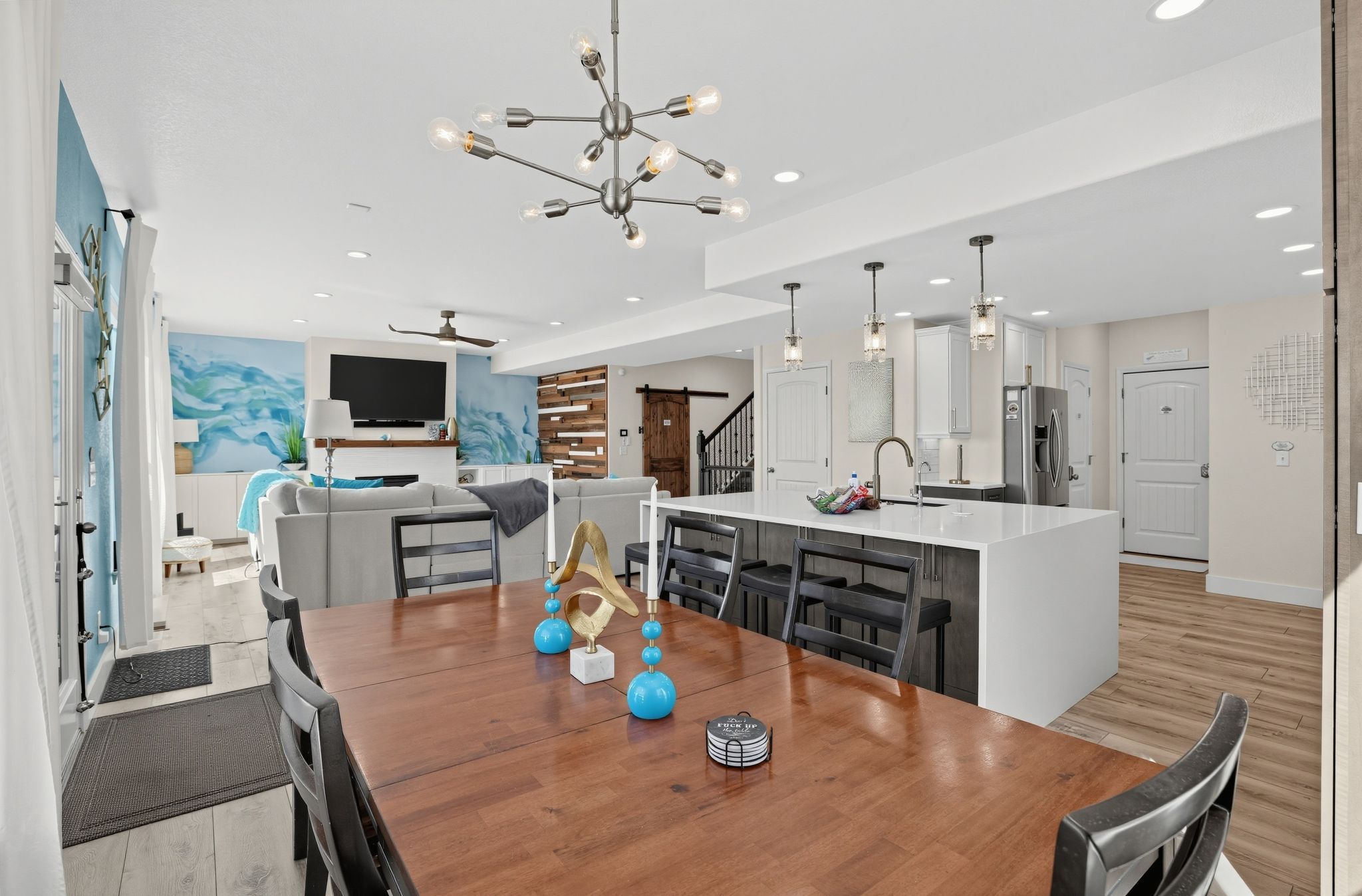 A modern kitchen with a central island, a dining area with a wooden table, and a living room with a sofa and TV.