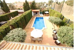 A swimming pool with a sun lounger and a table, surrounded by neatly trimmed hedges.