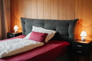 A bed with a grey headboard, red and white bedding, and two bedside lamps on wooden nightstands.