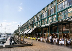 A waterfront restaurant with outdoor seating, a dock with boats, and a view of the marina. - Roslyn Studio Between Harbour Calm and City Energy (Potts Point)