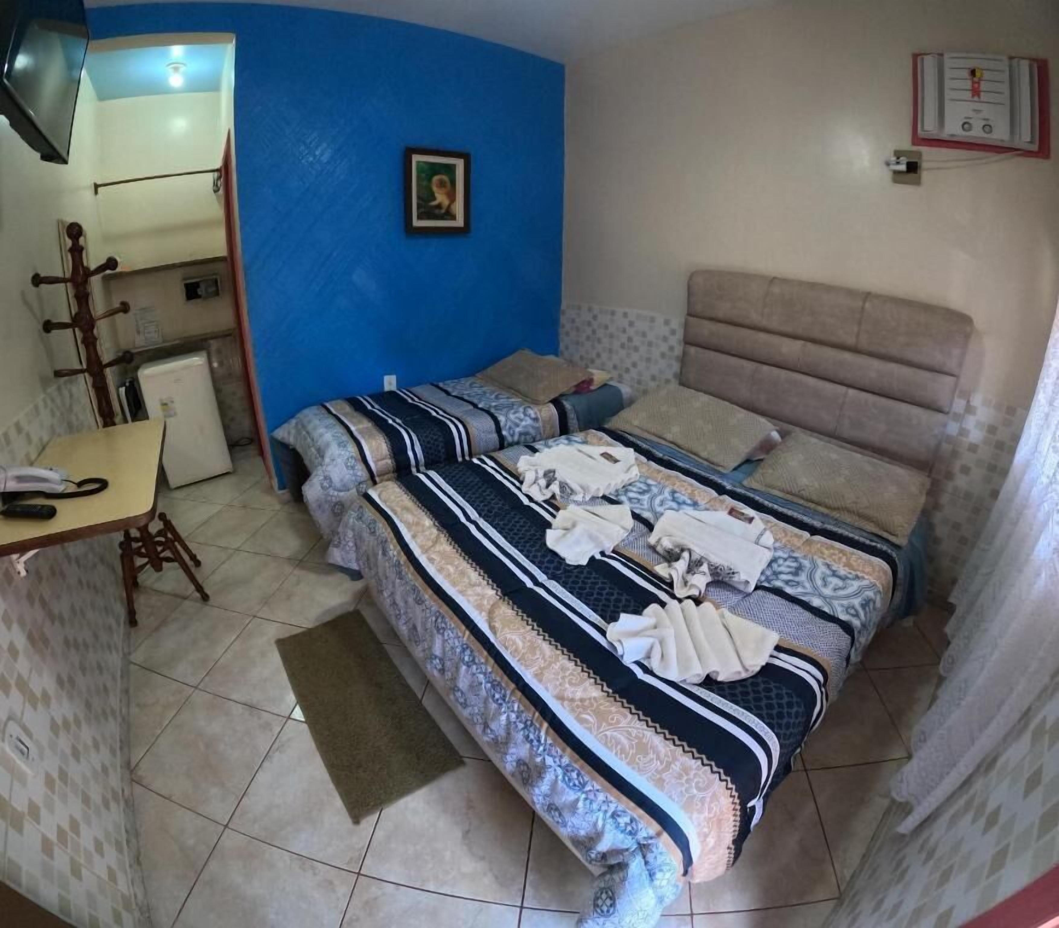 A room with a bed, a desk, a chair, a telephone, and a wall-mounted heater.