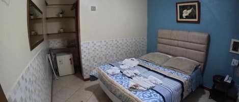 A bedroom with a bed, a ceiling fan, a small desk, and a wall-mounted TV.