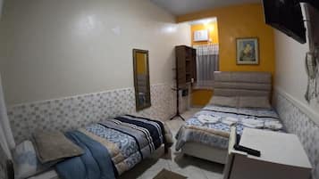 Quarto com duas camas, ventilador de teto, TV na parede e uma escrivaninha.