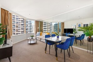 A modern living room with a sofa, coffee table, and dining area. - The Rocks Harbour Escape Resort Living and City View (Sydney)