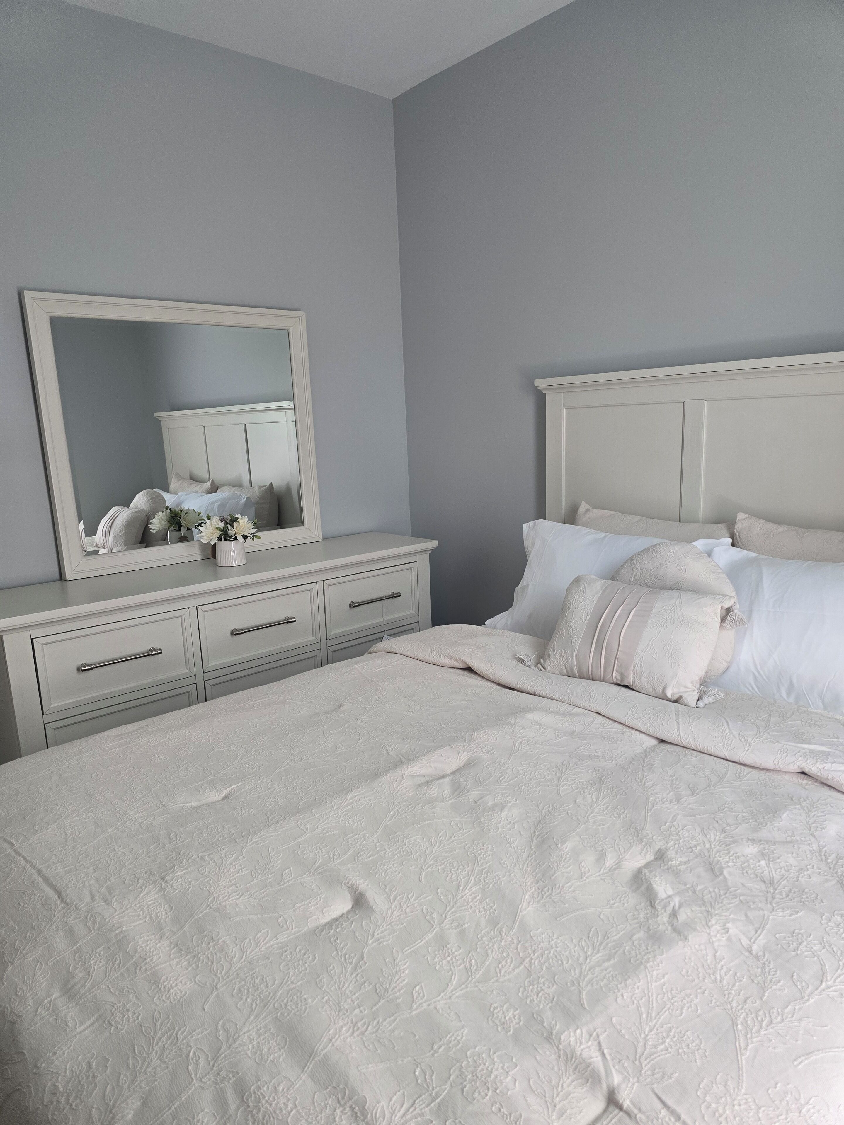 A bedroom with a large bed, a dresser with drawers, a mirror, and a bedside table.