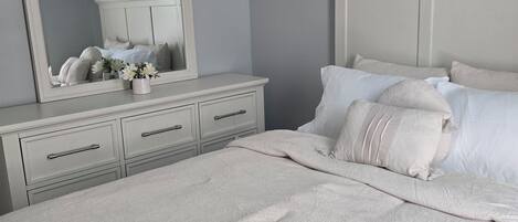 A bedroom with a large bed, a dresser with drawers, a mirror, and a bedside table.