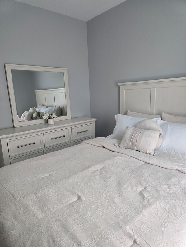 A bedroom with a large bed, a dresser with drawers, a mirror, and a bedside table.