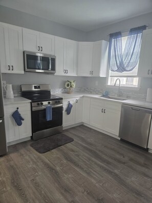 A modern kitchen with white cabinets, stainless steel appliances, and a wooden floor.