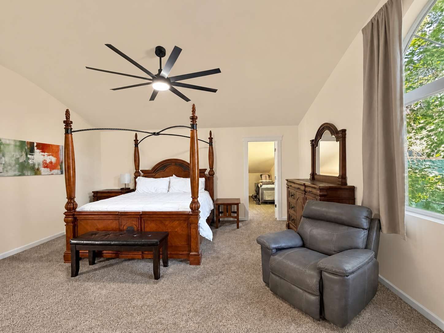 Ein Schlafzimmer mit Himmelbett, Deckenventilator, Ledersessel und Kommode.