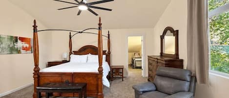 A bedroom with a four-poster bed, a ceiling fan, a leather armchair, and a dresser.