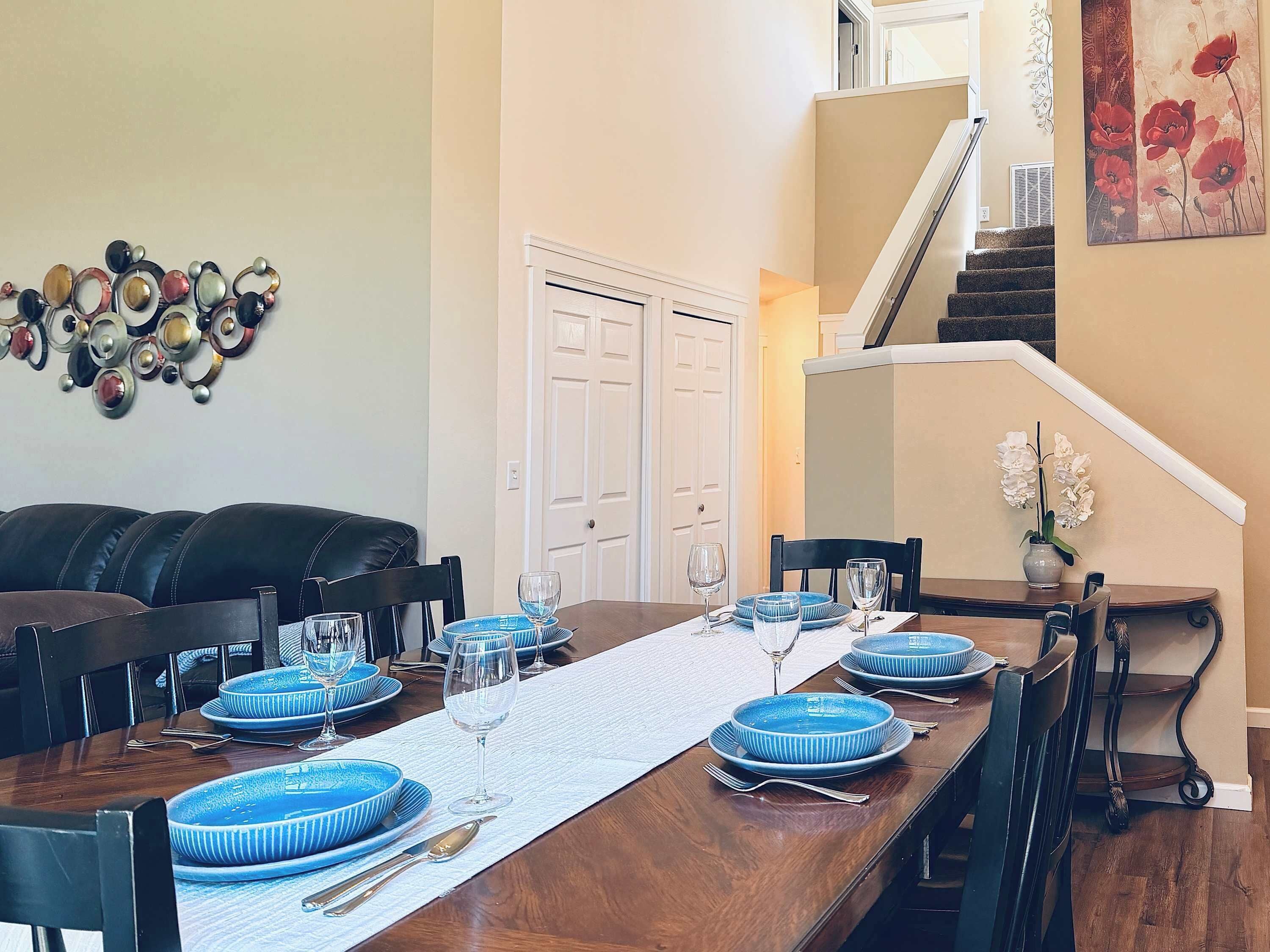 Un coin repas avec une table en bois dressée pour quatre personnes, des assiettes bleues et un set de table blanc.