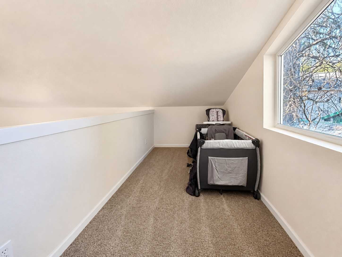 Une chambre d’angle avec une fenêtre, un berceau et un sol recouvert de moquette.