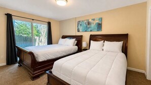 A hotel room with two double beds, a large window with curtains, a ceiling light, and a painting on the wall. - Unwind at Midtown Haven (Coeur d'Alene)