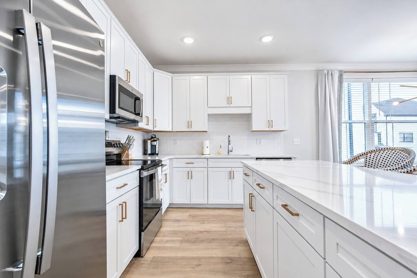 A modern kitchen with white cabinetry, stainless steel appliances, and a large island.