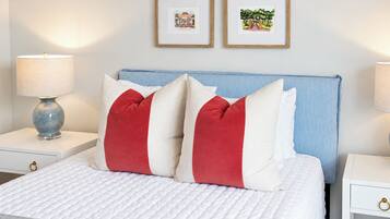 Una cama bien hecha con ropa blanca y almohadas rojas y blancas, flanqueada por dos mesitas de noche con lámparas y cuadros en la pared.