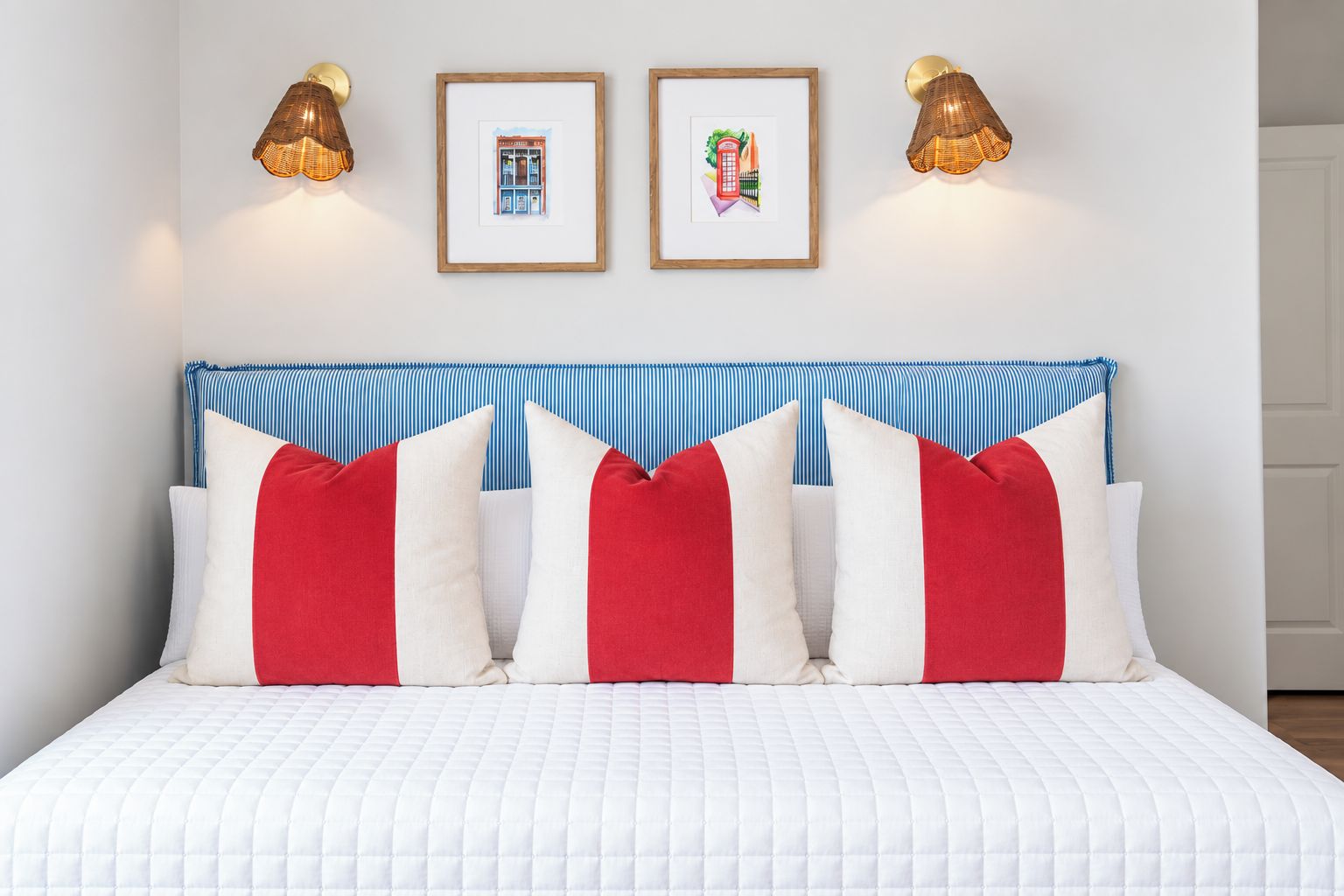 Uma cama com cobertura branca acolchoada, cabeceira listrada em azul e branco e almofadas vermelhas e brancas.