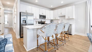 Una cocina moderna con armarios blancos, electrodomésticos de acero inoxidable y una isla central con taburetes de bar.