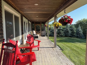A covered porch with red Adirondack chairs, a wooden table, and hanging flower baskets.