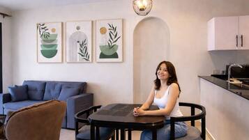 A modern living room with a sofa, a round table, and chairs. There are wall-mounted artworks and a ceiling light fixture.