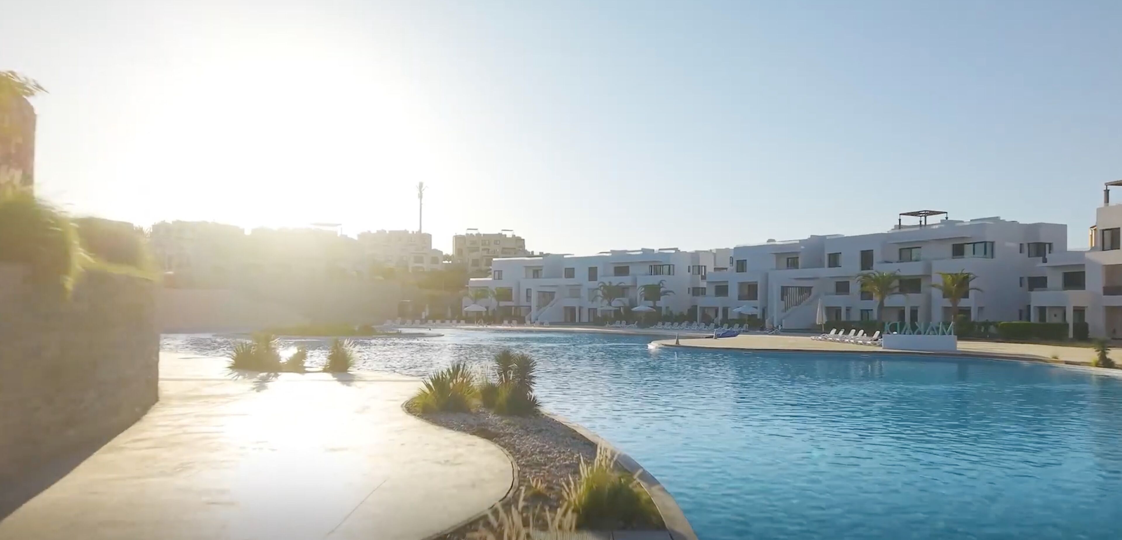 A resort with a swimming pool, modern buildings, and a clear sky.