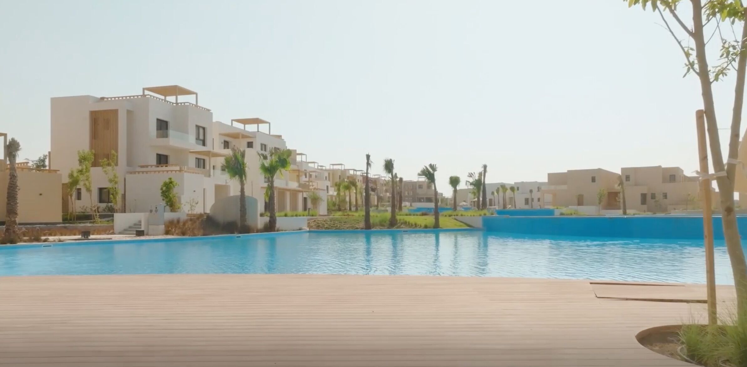 A swimming pool with a wooden deck, surrounded by modern buildings with balconies.