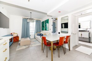 A modern living room with a dining area, a sofa, a TV, and a kitchen area with a mirror. - Stylish Beach Condo in the Heart of South Beach (Miami Beach)
