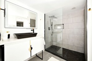 A modern bathroom with a glass-enclosed shower, a black vessel sink, and a large mirror. - Stylish Beach Condo in the Heart of South Beach (Miami Beach)
