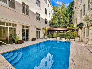 A swimming pool with steps leading into it, surrounded by a building with multiple windows and potted plants. - Spacious Newly Renovated Corner Unit South Beach (Miami Beach)