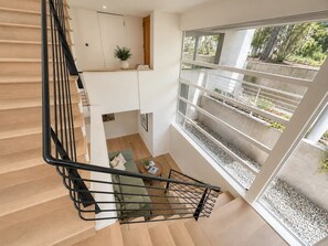 A modern interior with a staircase, a seating area, and a large window with a view of greenery.