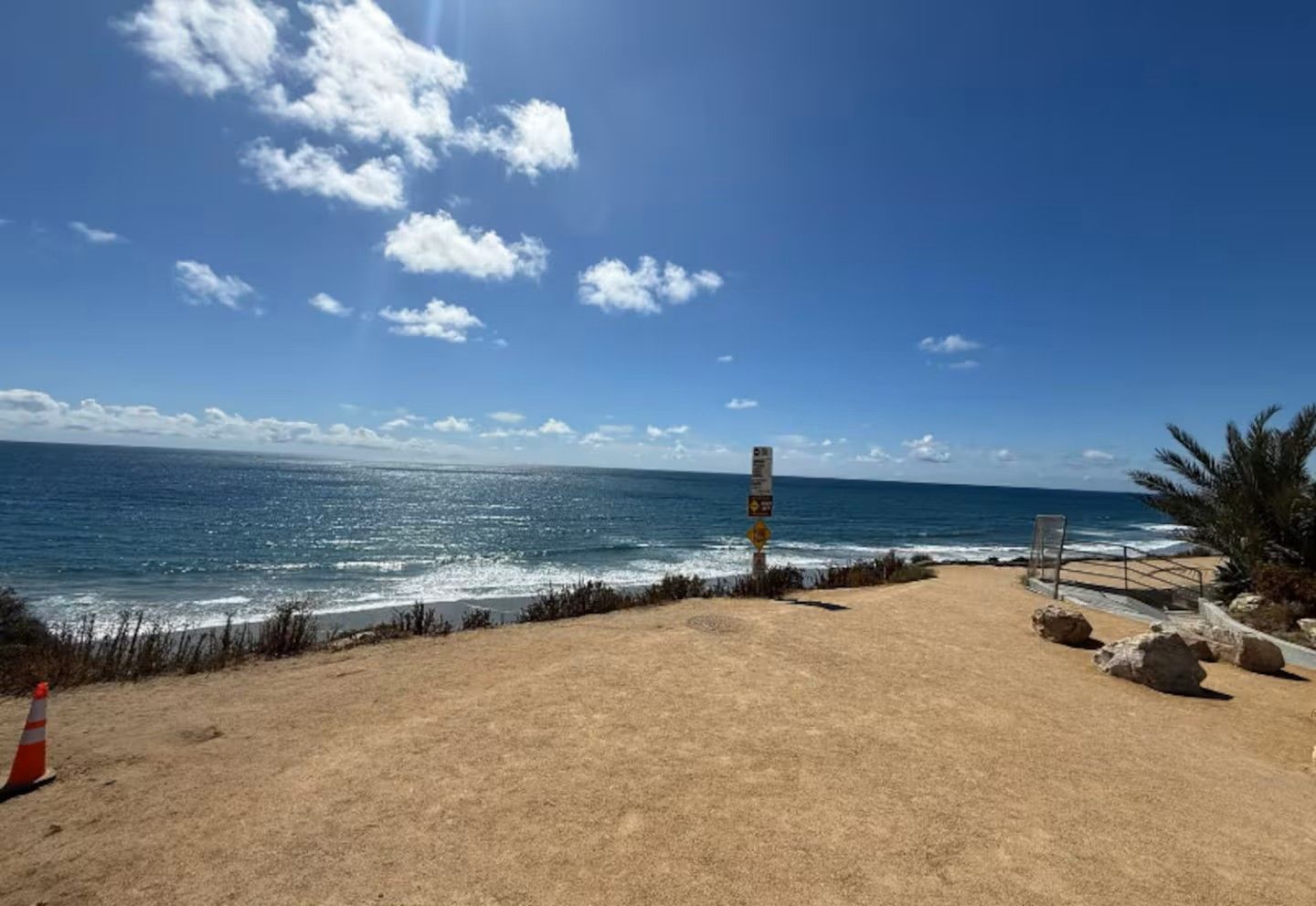 Una playa con cielo despejado, un camino arenoso que lleva al agua y una señal.