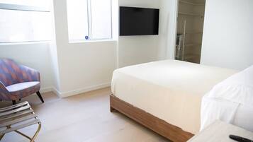 Un dormitorio con cama, una silla, televisor y zona de ducha.