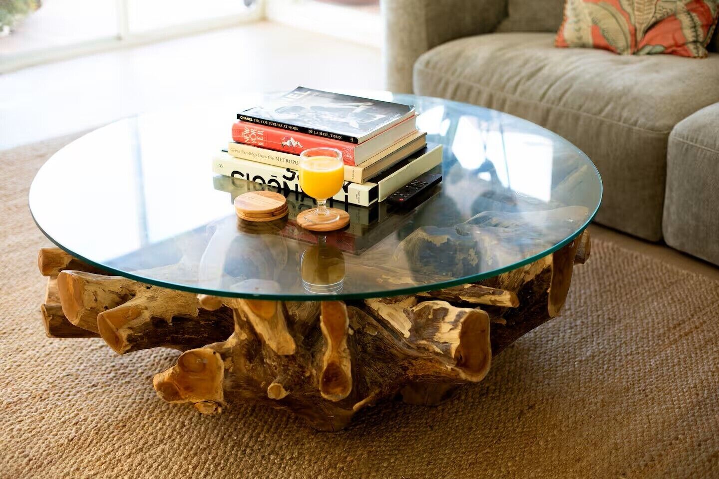 A round glass coffee table with a wooden base, a stack of books, and two glasses of orange juice.