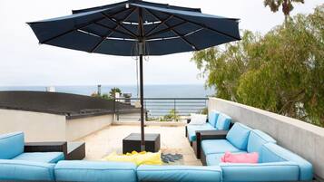 Una terraza en la azotea con un juego de sofá azul, un paraguas grande y vistas al mar.