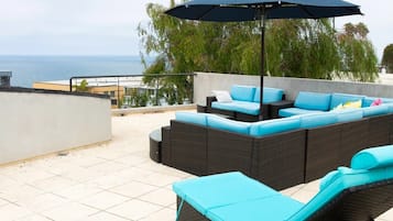 An outdoor seating area with a pool, a large umbrella, and a view of the ocean.