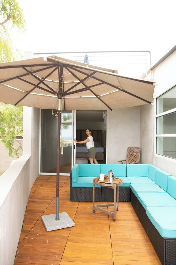 Un espace de détente extérieur moderne, comprenant un canapé d’angle, une table et un grand parasol.
