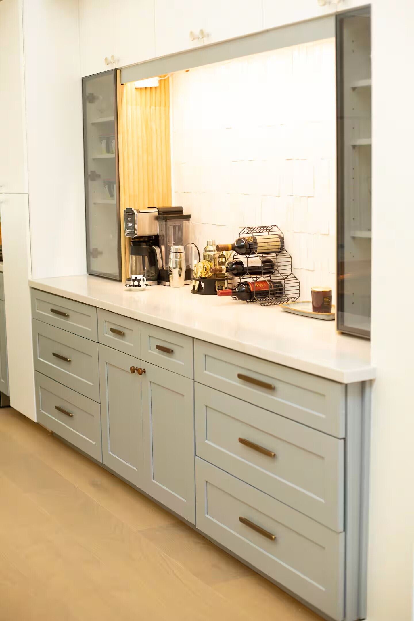 Una cocina con encimera blanca, cafetera, enfriador de vino y estante para vinos.